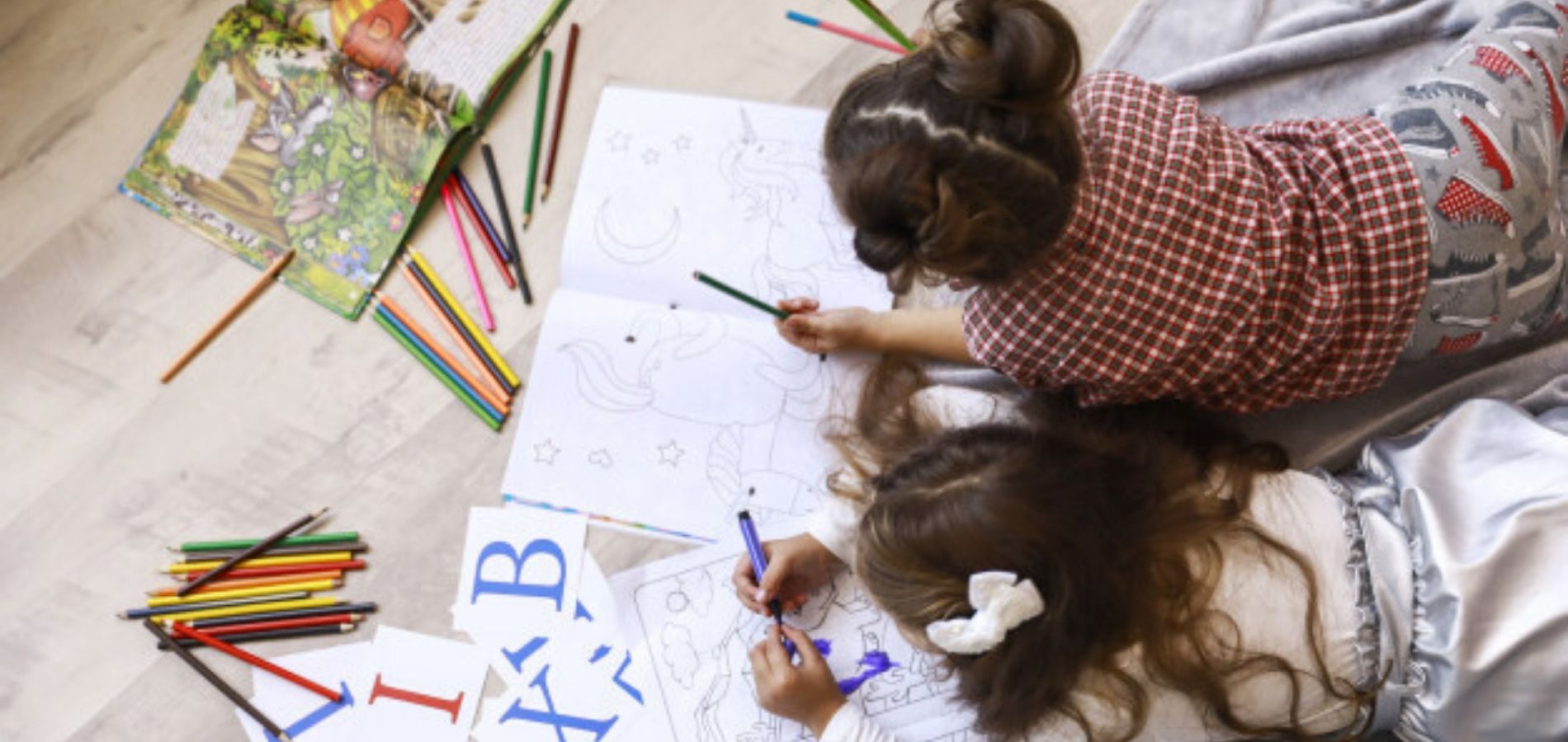 Dos niñas pequeñas jugando en el piso de su casa con lapices de colores, cuentos y letras del abecedario